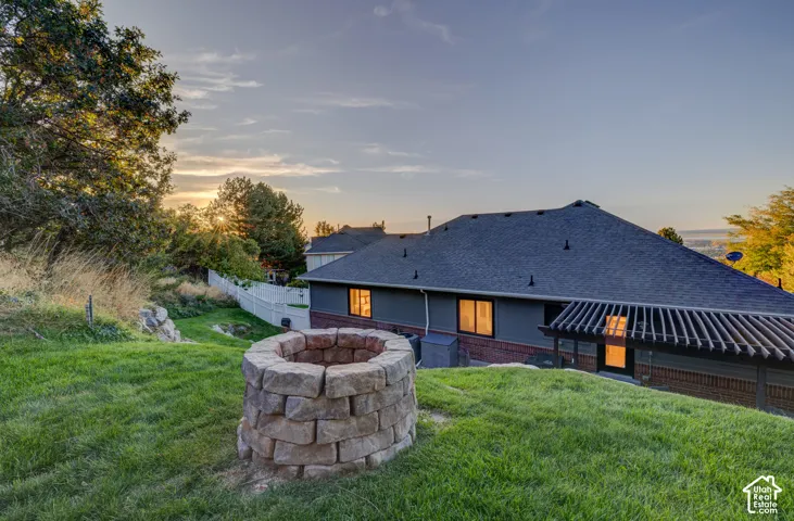 Expansive backyard featuring a stone fire pit, mature trees, and a slatted pergola structure