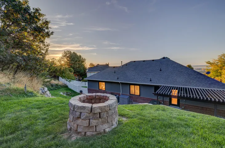 Expansive backyard featuring a stone fire pit, mature trees, and a slatted pergola structure