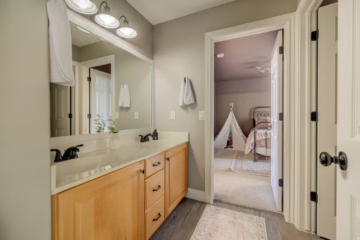 Double vanity with black fixtures, light wood-finish cabinetry, and a full-width mirror