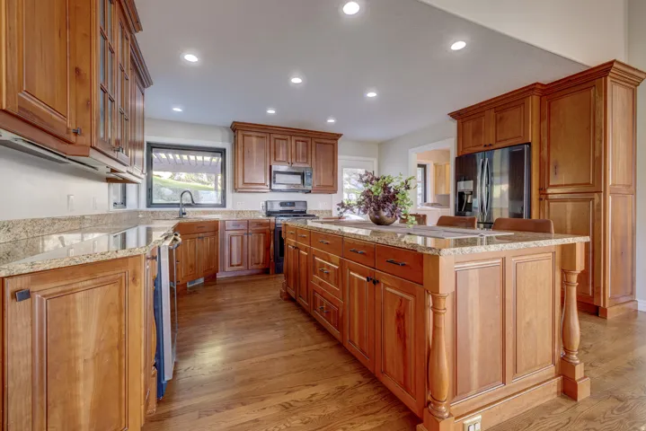 Kitchen featuring wood cabinetry, granite countertops, a large center island with seating, a built-in refrigerator, and wood-finish flooring