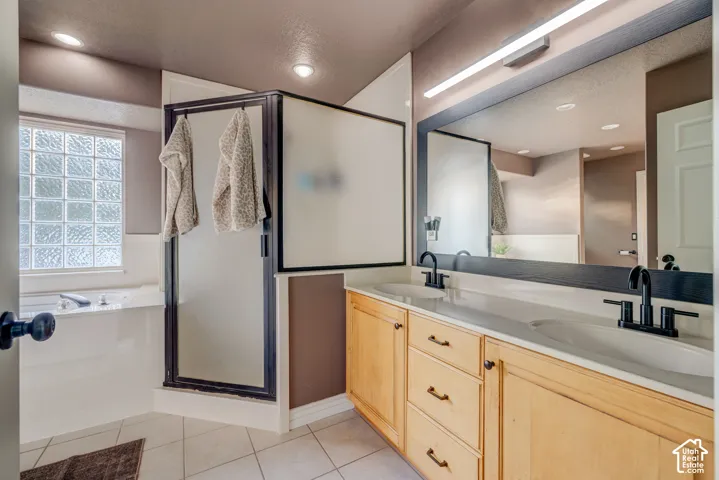 Dual vanity with integrated sinks and matte black fixtures, full-width mirror, light wood-finish cabinetry, tile flooring, and a glass block window