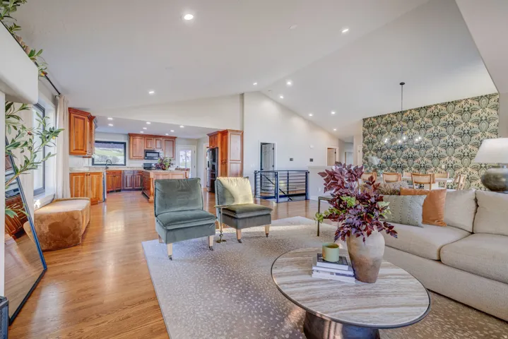 Open-concept living area with vaulted ceilings, recessed lighting, wood-finish flooring, and a kitchen featuring wood cabinetry and an island