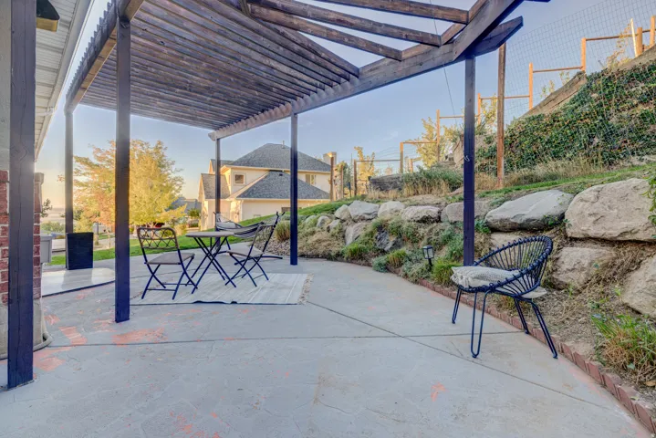 Expansive concrete patio featuring a wood pergola, brick accents, and a tiered rock retaining wall with established plantings