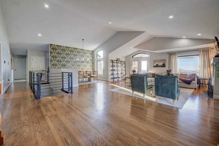 Wood-finish flooring throughout, modern stair railing, vaulted ceiling, recessed lighting, and expansive windows