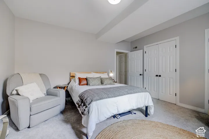 Soft neutral wall color, recessed ceiling beam, carpet flooring, dual paneled closet doors, and wood-toned bed frame