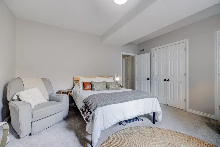 Soft neutral wall color, recessed ceiling beam, carpet flooring, dual paneled closet doors, and wood-toned bed frame