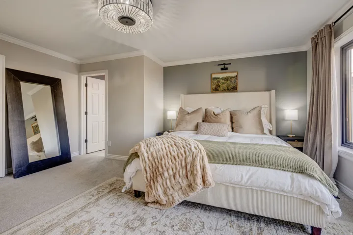 Plush carpeting with an inset area rug, crown molding, a crystal flush mount light fixture, and a window with custom drapery
