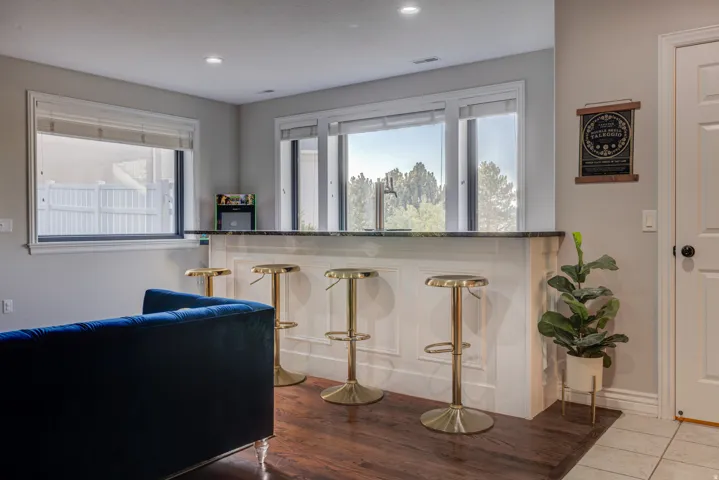 Built-in bar with a dark countertop and paneled base, recessed lighting, and wood-finish flooring