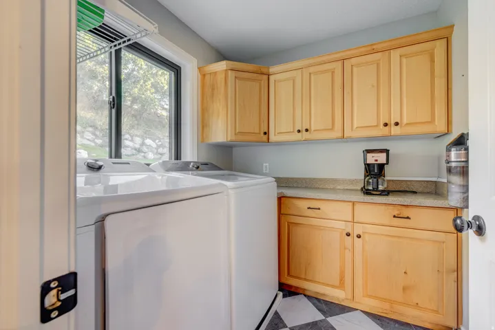 Light wood-finish cabinetry, solid surface countertop, and black and white checkered flooring