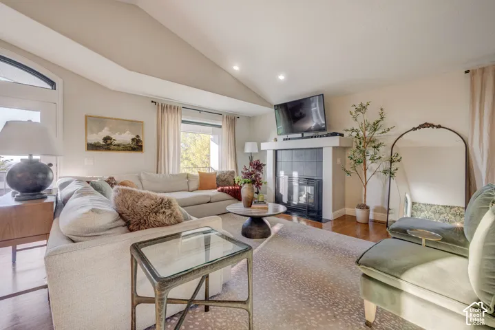 Vaulted ceiling with recessed lighting, integrated fireplace with dark tile surround and white mantel, wood-finish flooring, and large windows