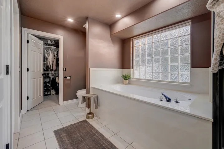 Built-in soaking tub with deck-mounted fixtures, glass block window, recessed lighting, and tile flooring