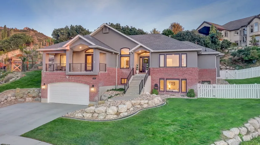 Multi-level residence featuring a brick and stucco exterior, an attached garage, and a covered balcony with a metal railing