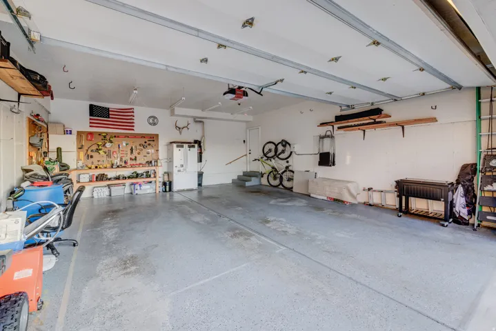 Spacious garage with an epoxy-finished floor, overhead door, built-in shelving, and utility sink