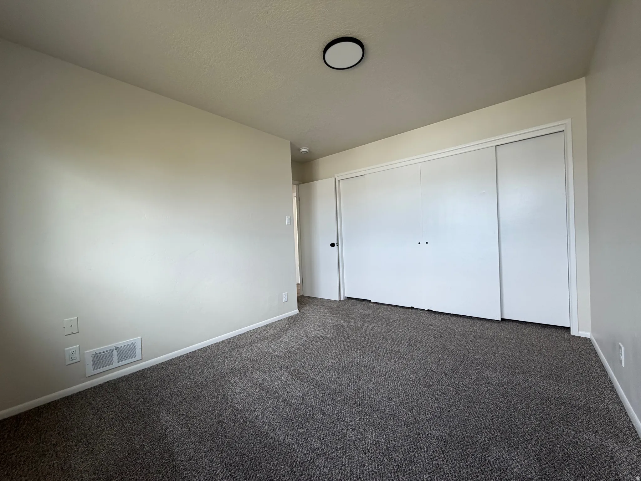 Plush carpet flooring, a flush-mount ceiling light, and ample closet space with bi-fold doors