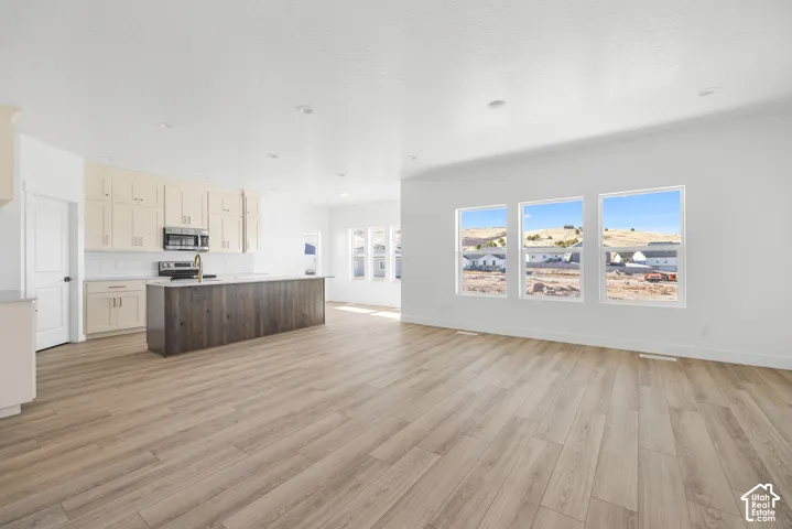 Open-concept living space featuring wood-finish flooring, a kitchen island with a wood-finish base, ample cabinetry, and three large windows