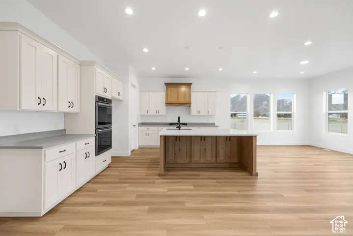 Open-concept kitchen featuring wood-finish flooring, white cabinetry, a kitchen island with seating, a double wall oven, and recessed lighting