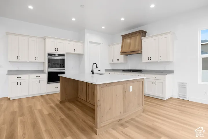 White cabinetry, wood-finish flooring, light-toned island with integrated sink, black matte faucet, and dual wall ovens