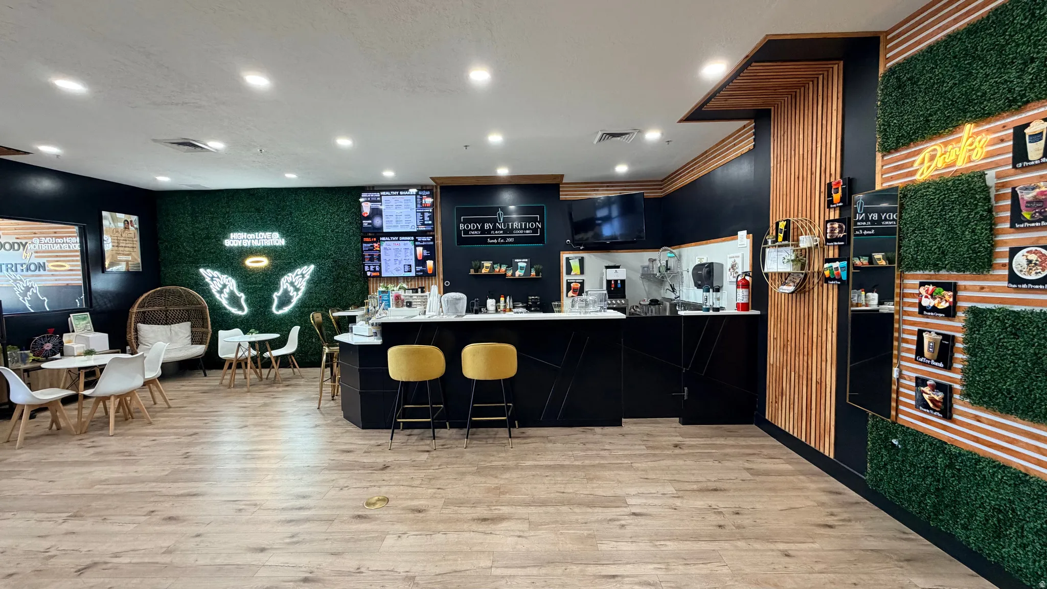 Wood-finish flooring with a dark wood-paneled accent wall, and a green artificial turf wall with a neon light fixture