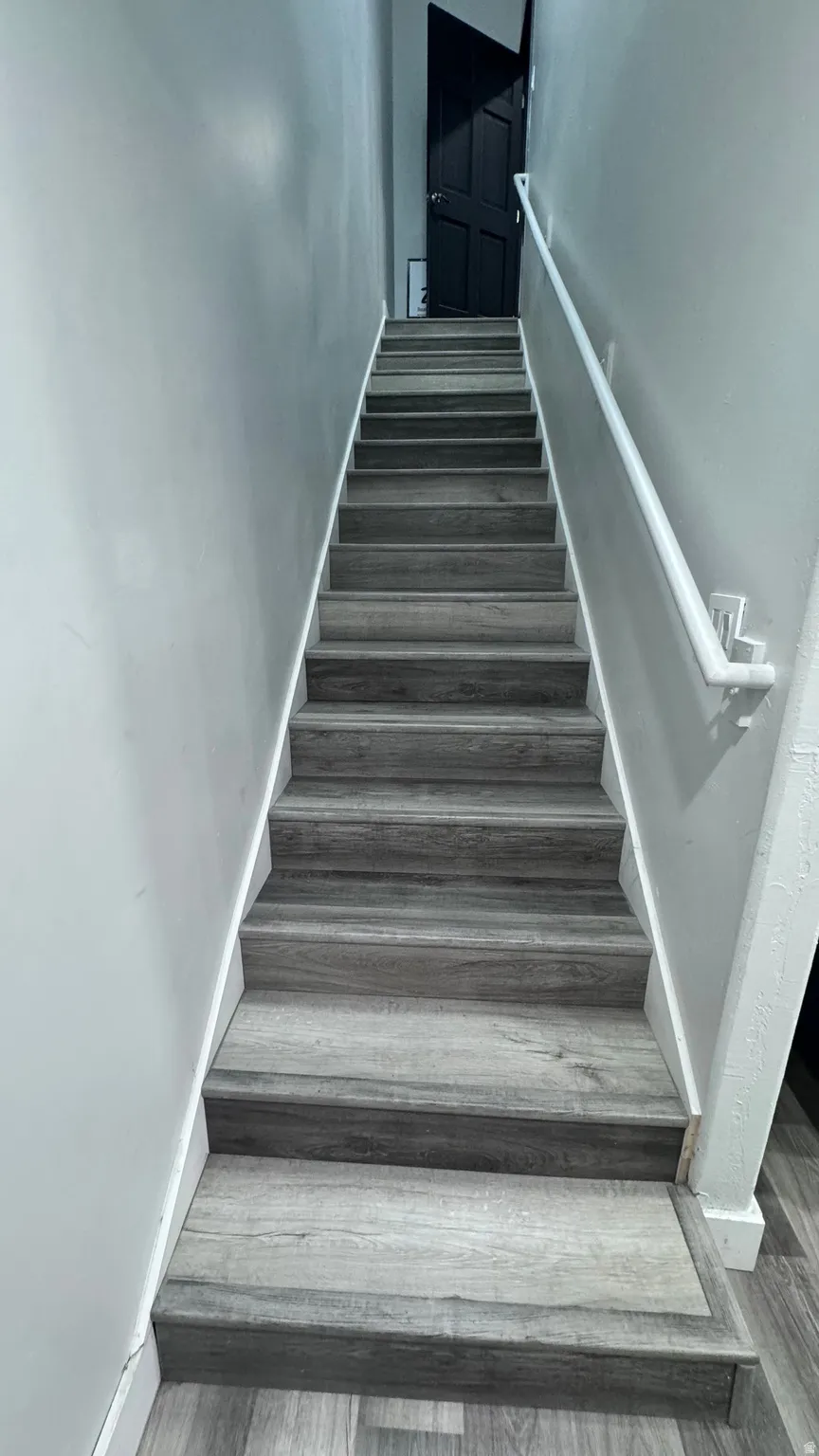 Staircase featuring wood-finish treads and risers, white handrail, and light gray wall paint
