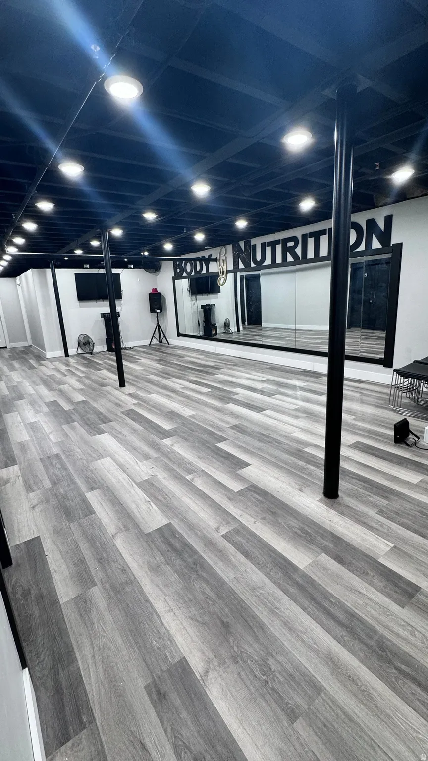 Spacious room featuring wood-finish flooring, recessed ceiling lighting, full-height wall mirrors, and exposed ceiling joists