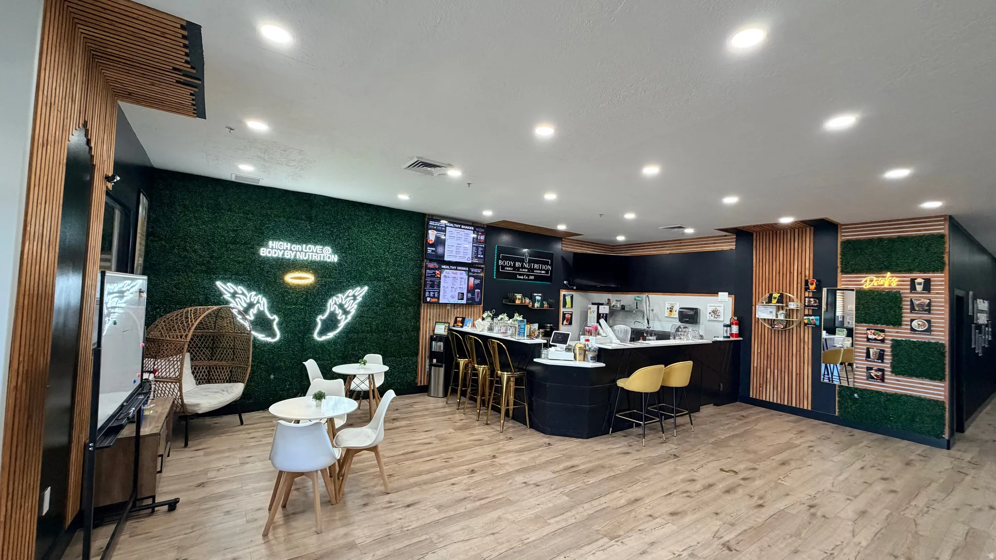 Wood-finish flooring throughout, featuring a service counter with built-in shelving, recessed ceiling lighting, and decorative wall treatments including a faux-grass wall and slatted wood panels