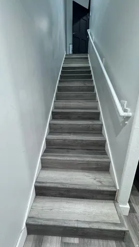 Staircase featuring wood-finish treads and risers, white handrail, and light gray wall paint