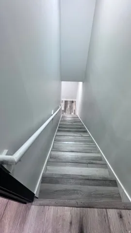 Staircase with wood-finish treads and risers, light gray wall paint, and a white handrail