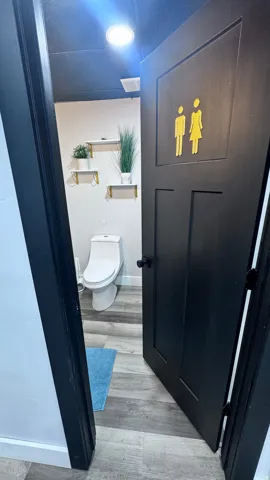 White toilet with a built-in bidet, wood-finish flooring, recessed lighting, and wall-mounted shelving