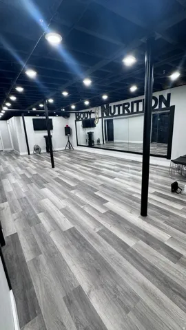 Spacious room featuring wood-finish flooring, recessed ceiling lighting, full-height wall mirrors, and exposed ceiling joists