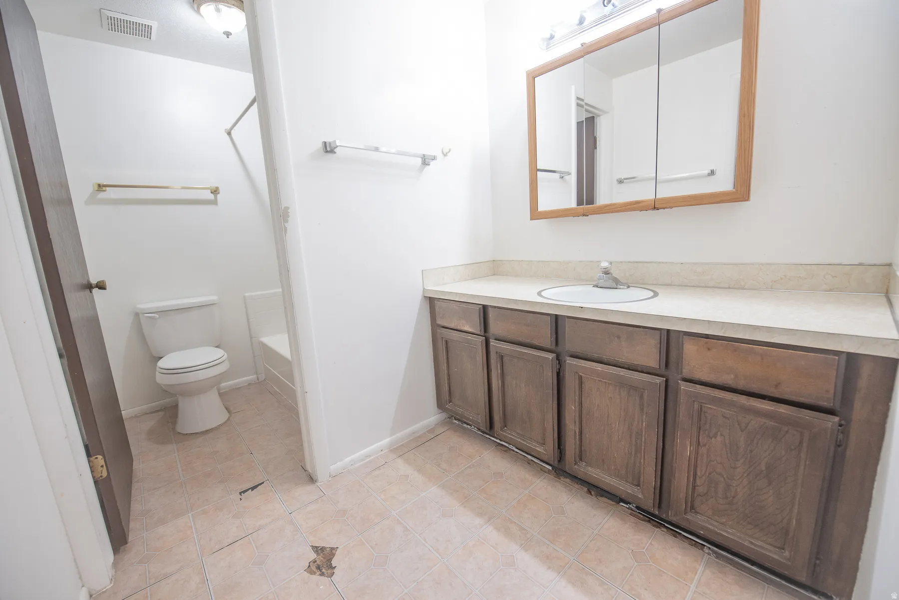 Bathroom featuring a wood-finish vanity with an integrated sink and an overhead mirrored medicine cabinet