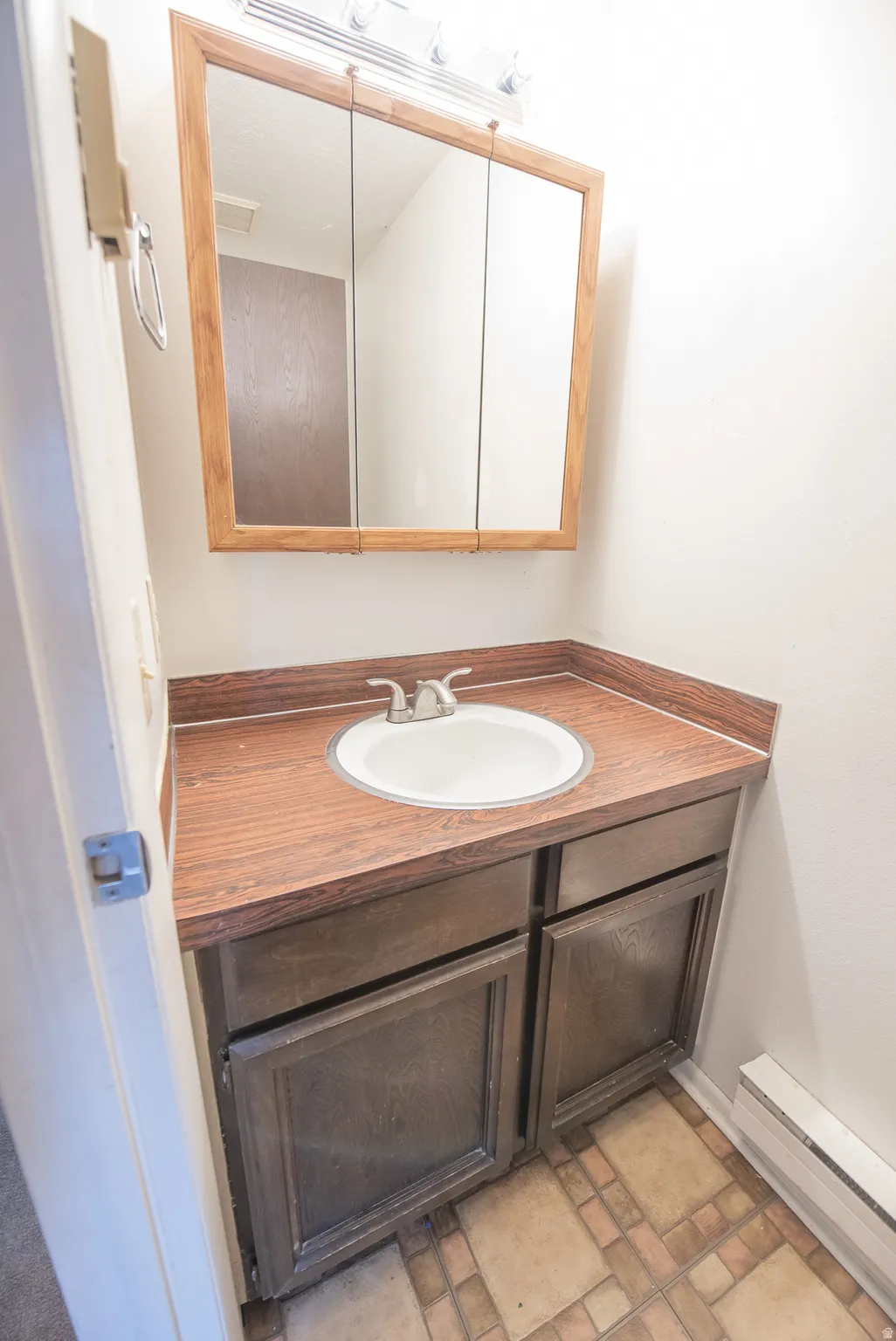 Vanity with a wood-finish countertop and an integrated sink, framed tri-fold mirror, and tiled flooring