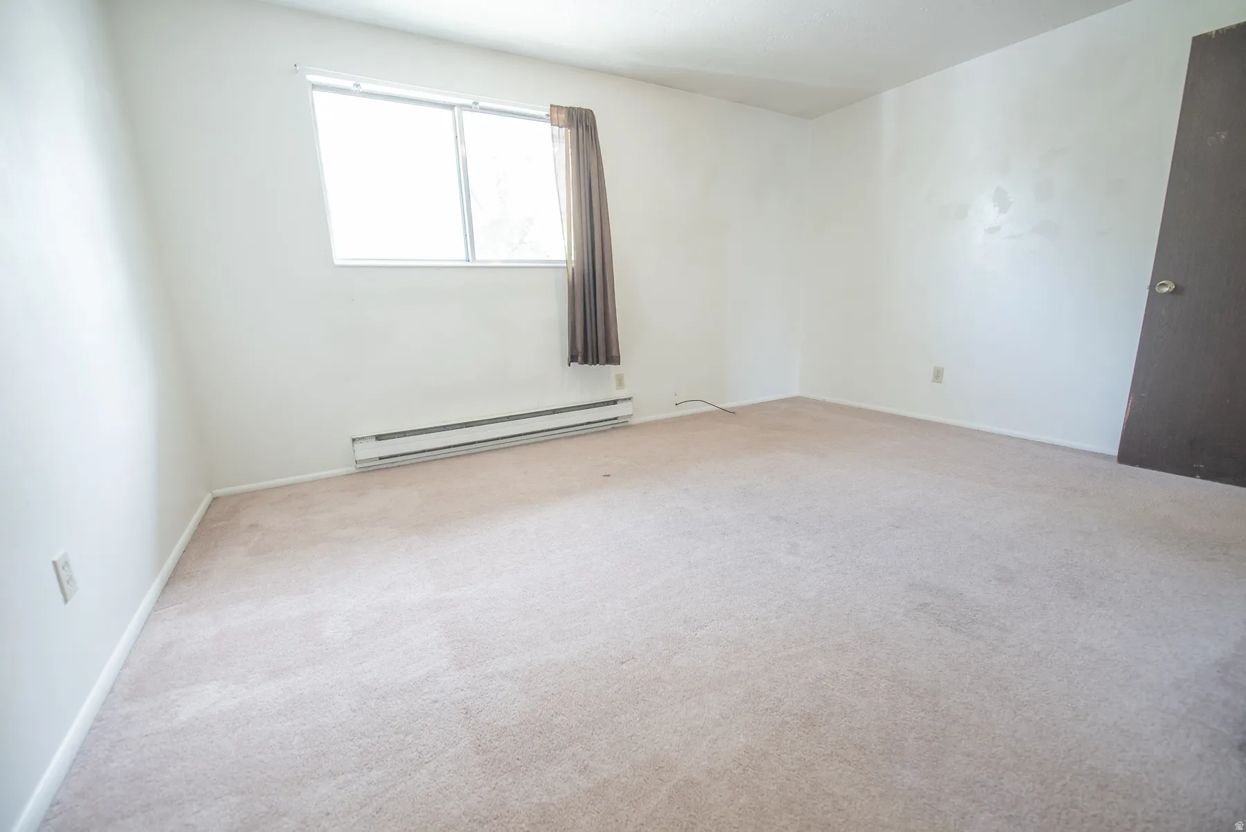 Light-colored carpeting with white walls, a large window, and baseboard heating