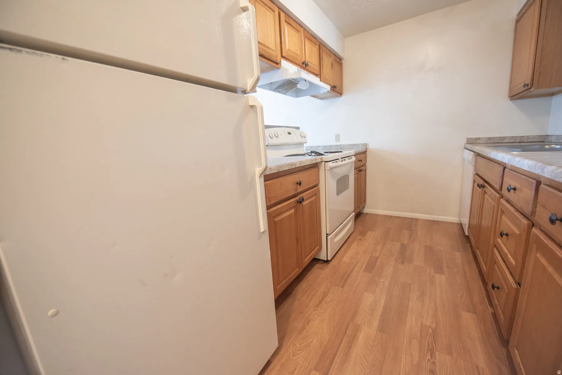 Kitchen featuring wood-finish flooring, light wood cabinetry, and a white appliance package