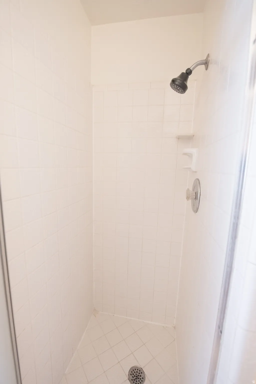 Walk-in shower with white tile surround, integrated soap dish, and a dark finish showerhead