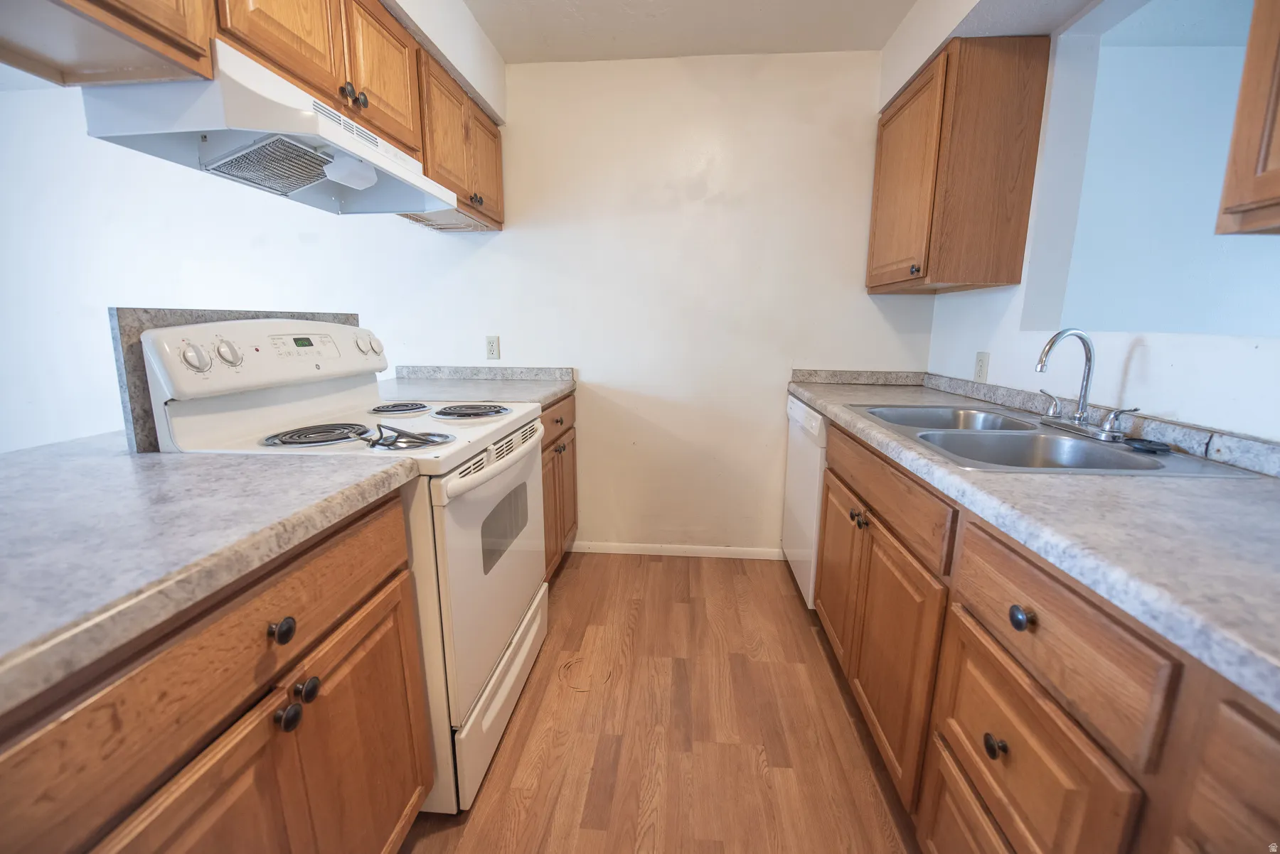 Kitchen featuring wood-finish flooring, wood cabinetry with dark hardware, a white electric range with a range hood, and a double basin stainless steel sink