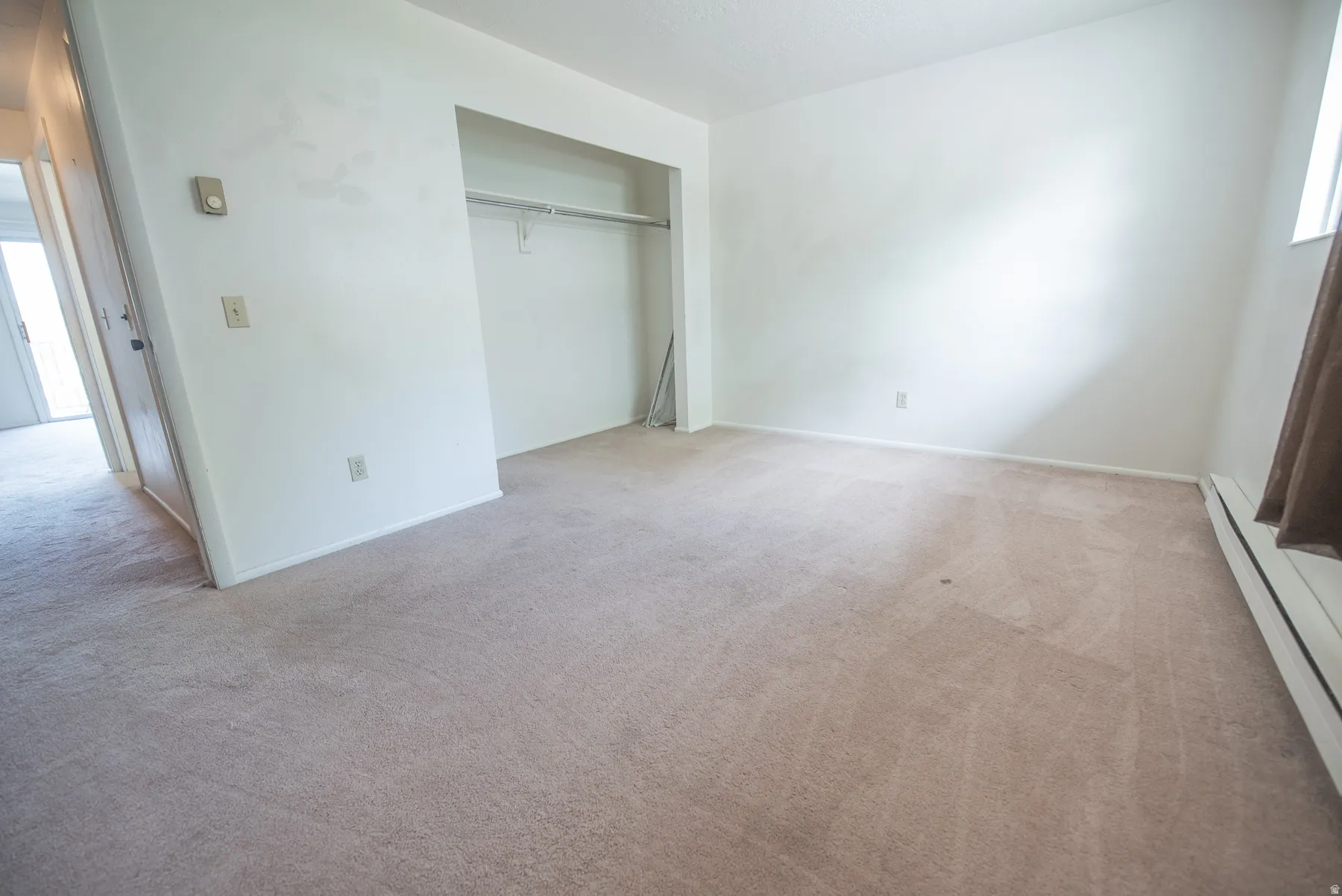 Carpeted flooring, built-in closet with hanging rod, window with curtain rod, and wall-mounted thermostat