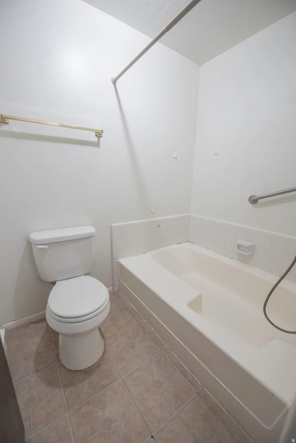 Full bathtub with integrated seating, white toilet, grab bar, and patterned floor tiling