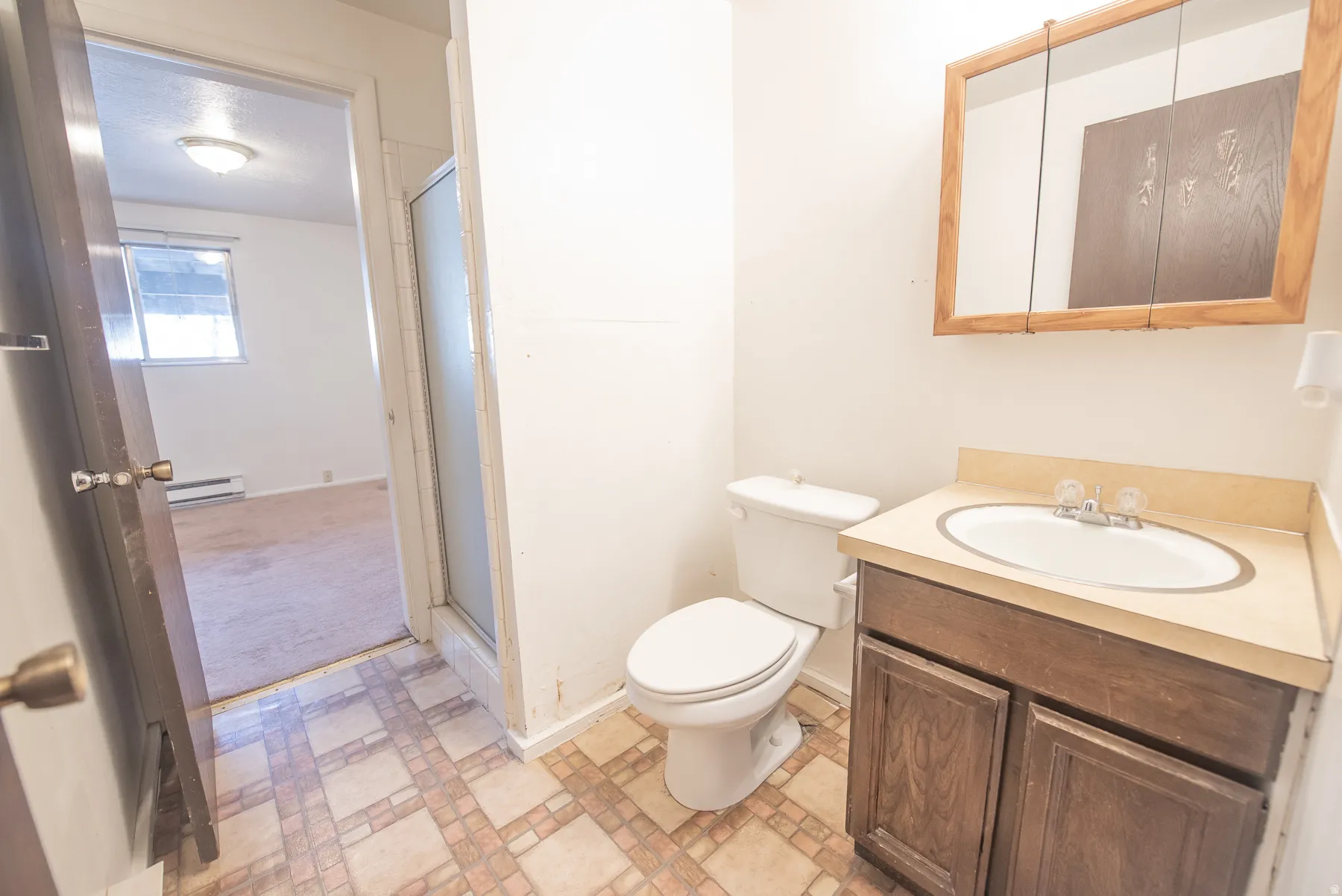 White toilet, wood-finish vanity with countertop and sink, framed medicine cabinet, and patterned floor tiling