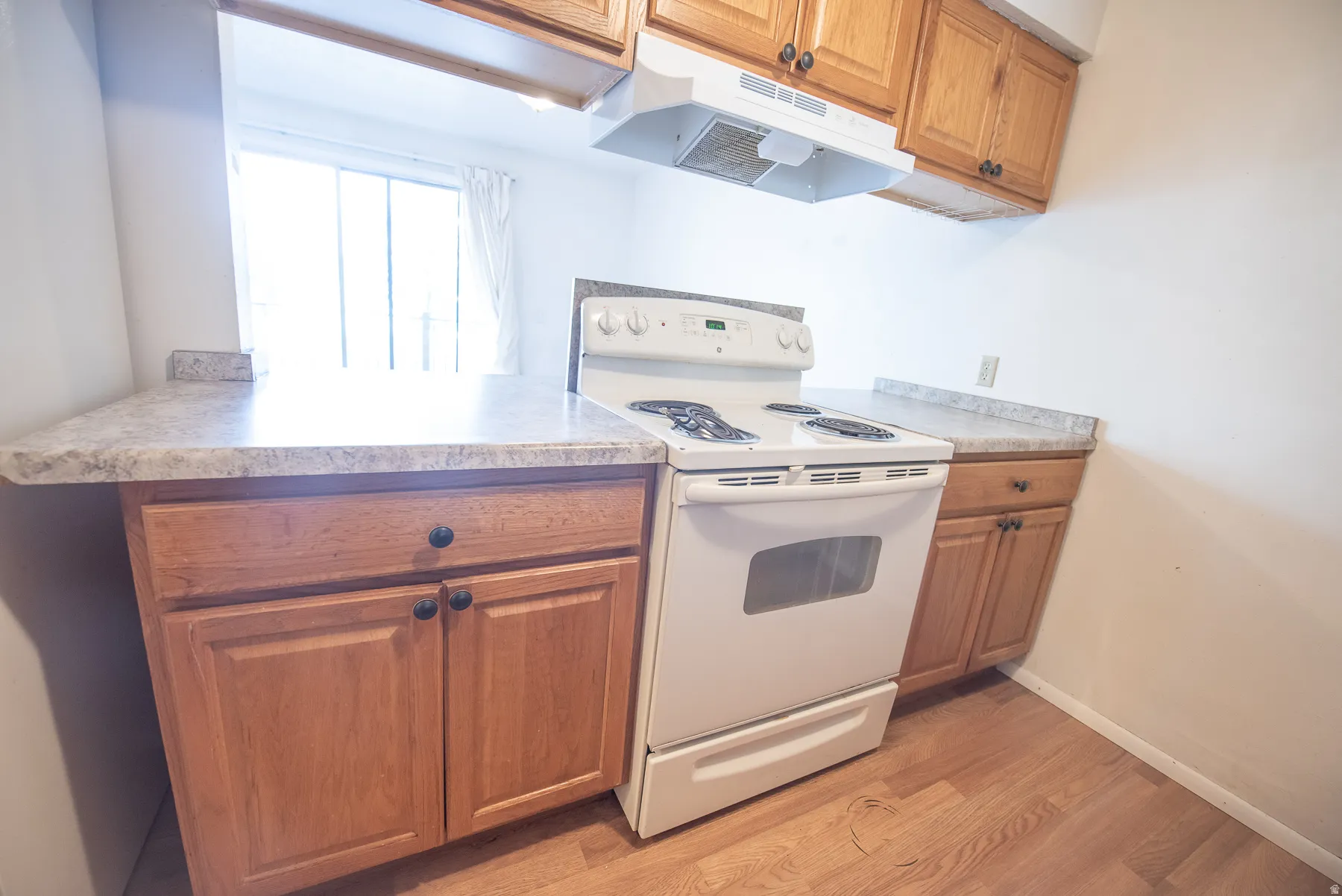 Kitchen featuring light wood-finish cabinetry, light-colored countertops, white electric range, and wood-finish flooring