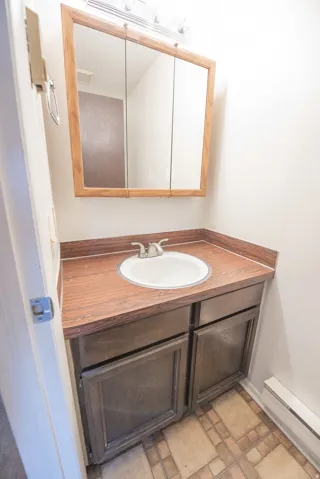 Vanity with a wood-finish countertop and an integrated sink, framed tri-fold mirror, and tiled flooring