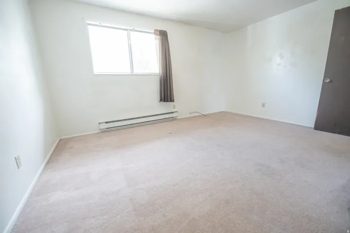 Light-colored carpeting with white walls, a large window, and baseboard heating