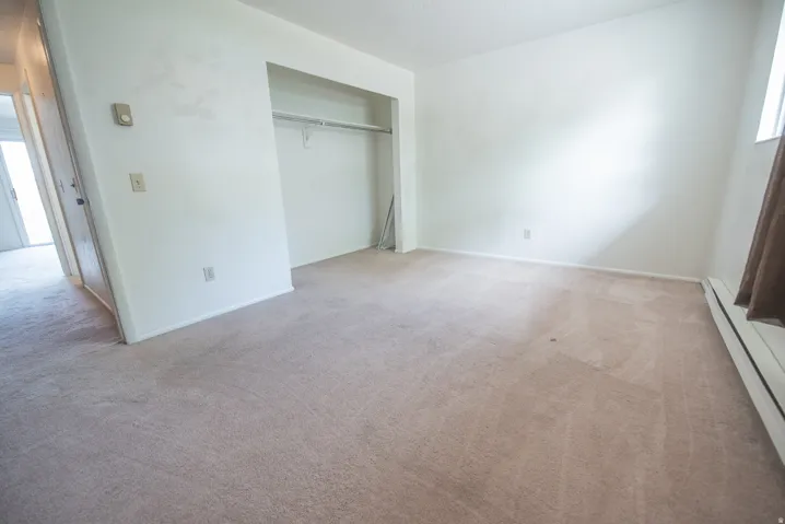Carpeted flooring, built-in closet with hanging rod, window with curtain rod, and wall-mounted thermostat