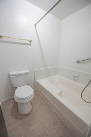 Full bathtub with integrated seating, white toilet, grab bar, and patterned floor tiling