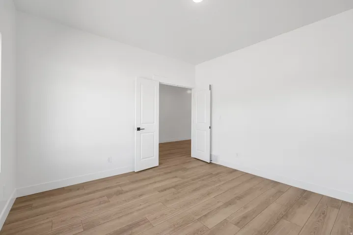 Bright, light-filled bedroom featuring pristine white walls, recessed ceiling lighting, and warm wood-finish flooring throughout
