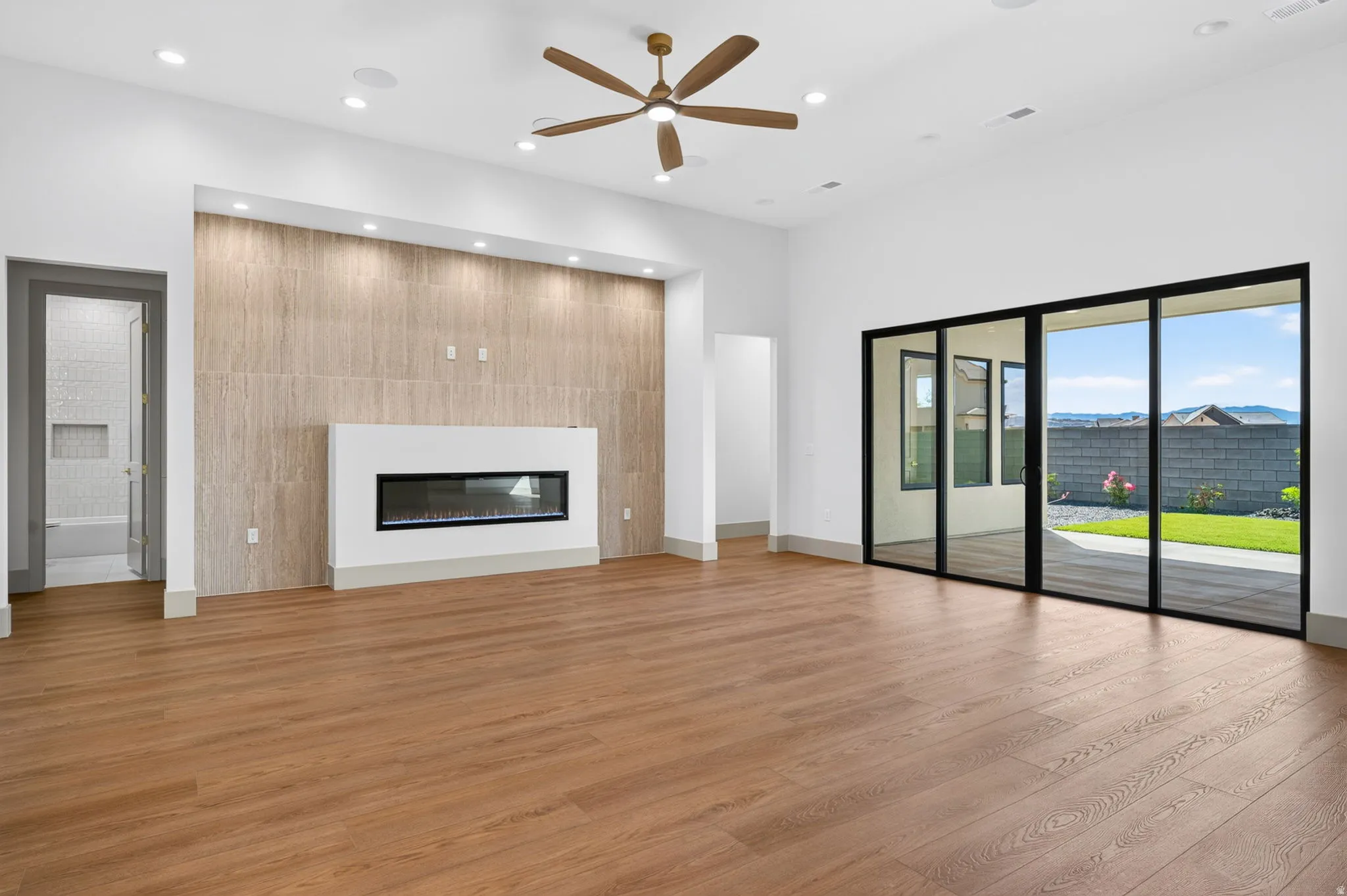 Recessed lighting, wood-finish flooring, a linear electric fireplace with tile surround, a ceiling fan, and black-framed sliding glass doors