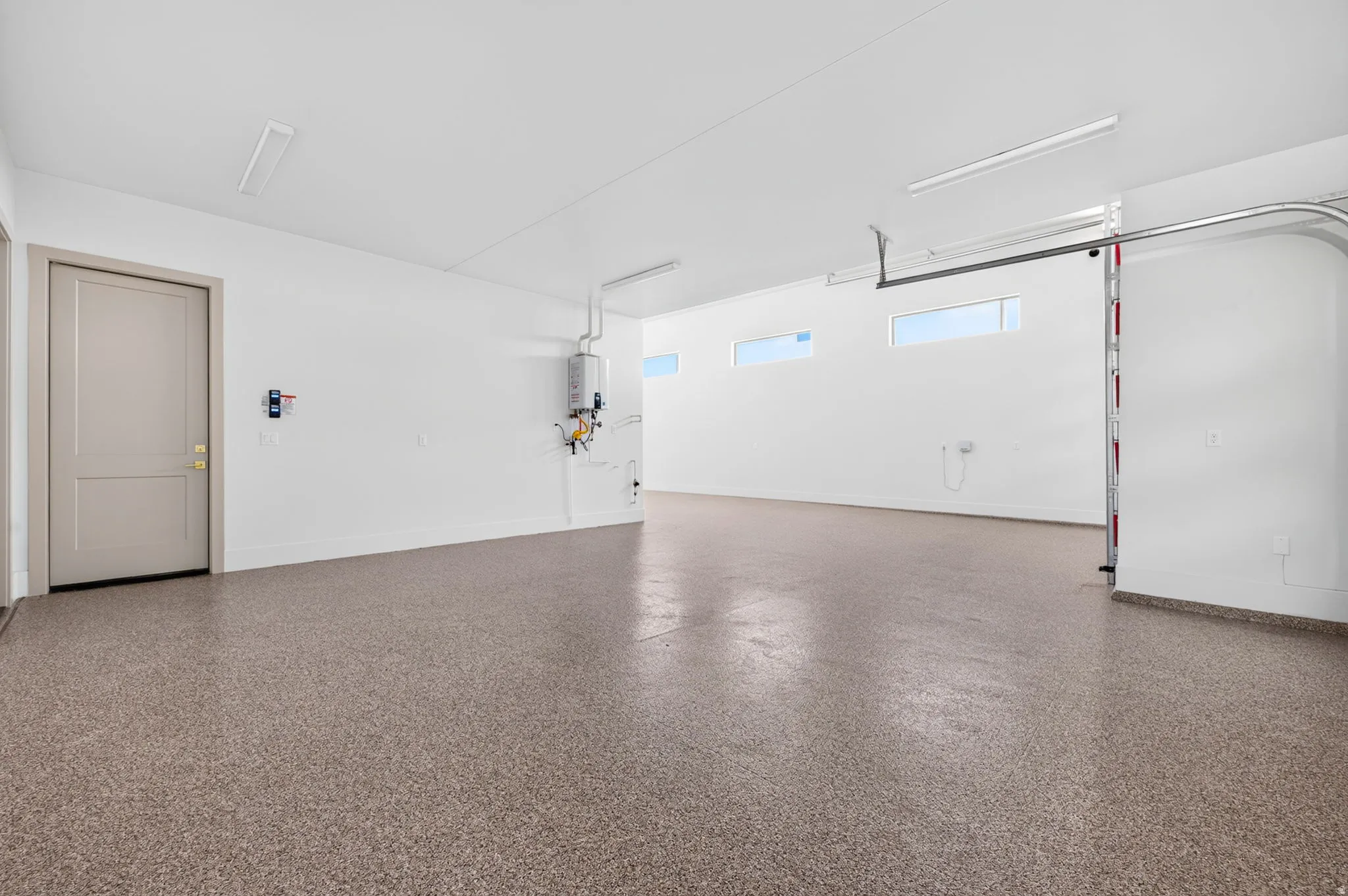 Spacious garage featuring a durable epoxy flooring, horizontal wall windows, and a tankless water heater