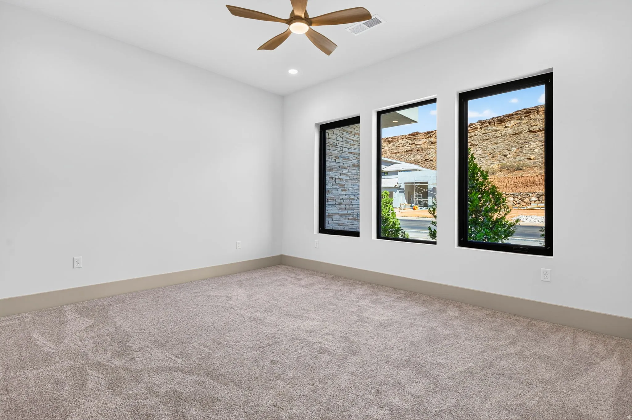 Recessed lighting, ceiling fan, and three large windows with dark frames