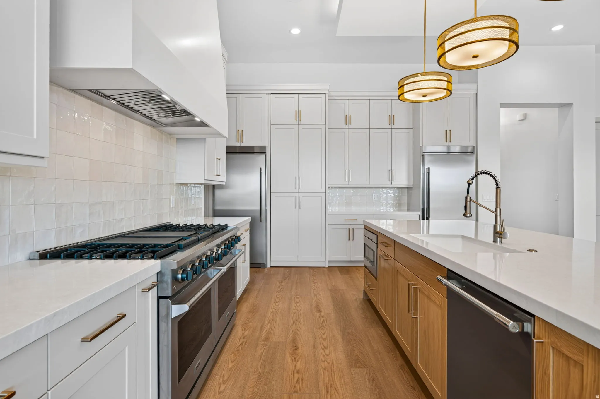 Gourmet kitchen with wood-finish flooring, white cabinetry, stainless steel appliances, a large island with sink, and decorative pendant lighting