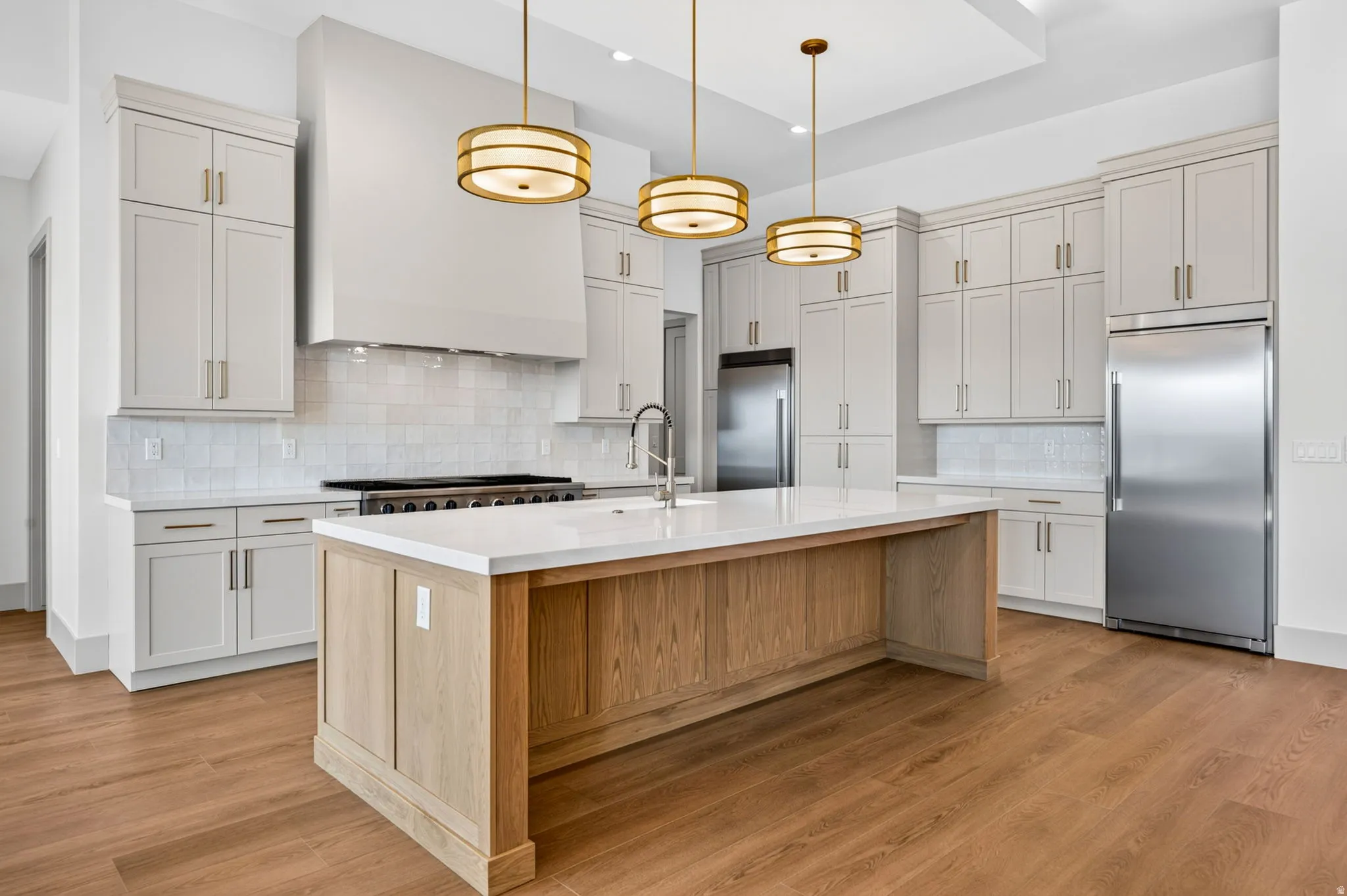 Expansive kitchen featuring wood-finish flooring, a large center island with a light wood finish, white countertops, and stainless steel appliances