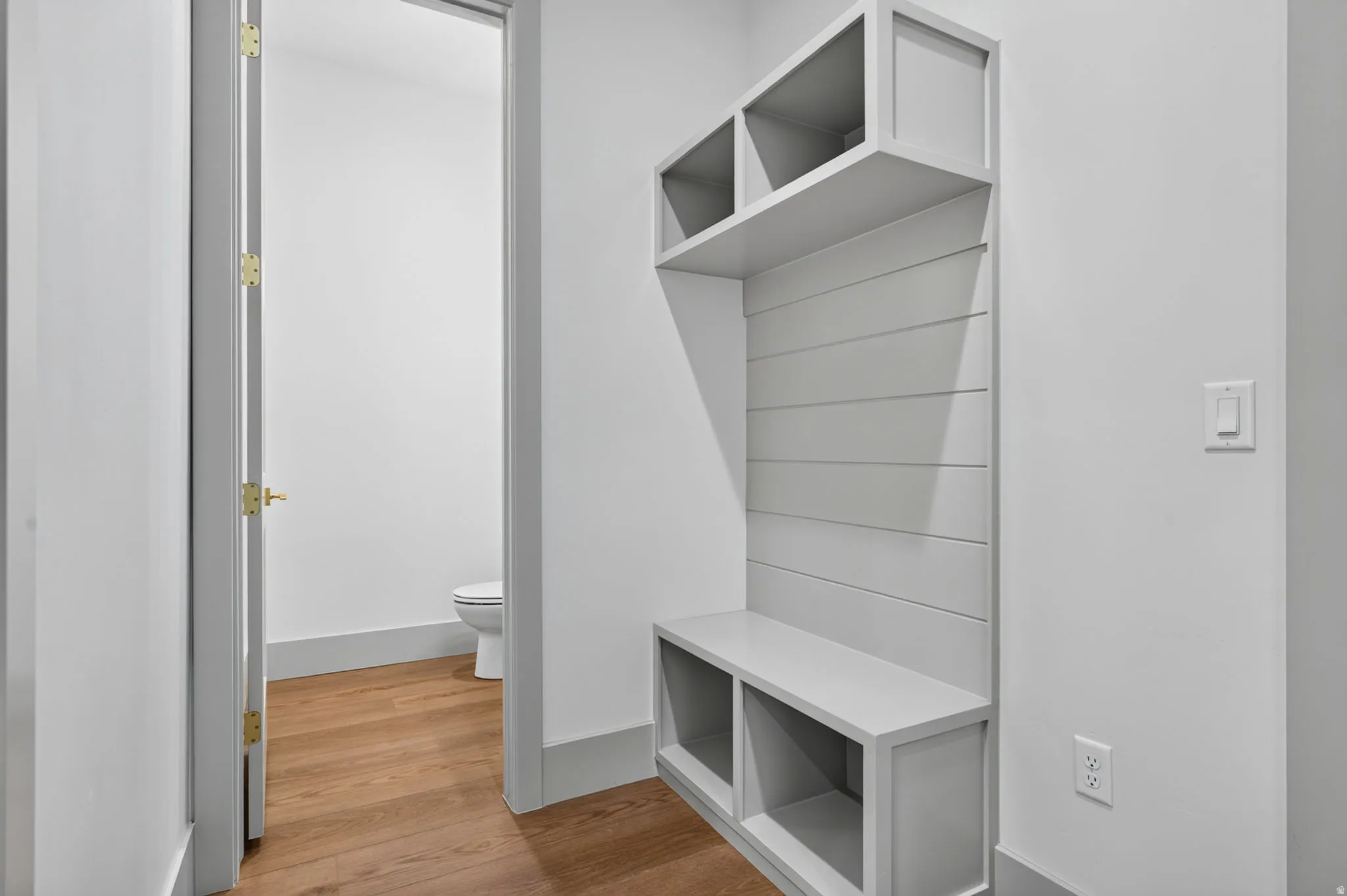 Built-in storage bench with open shelving, wood-finish flooring, and a white interior door
